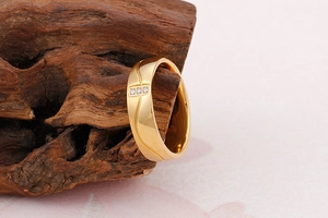 Détail d'une bague dorée ondulée avec trois zircons posée sur un bois flotté sombre