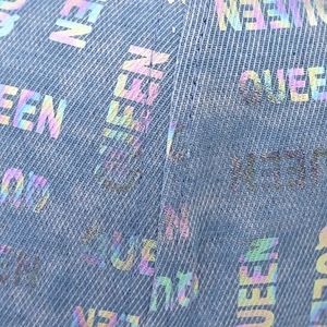 Dettaglio di denim azzurro con motivo a lettere QUEEN stampato al laser iridescente