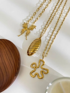 Detailed close-up of three gold titanium necklaces with butterfly and floral pendants