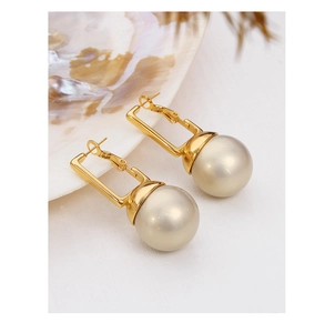 Détail de boucles d'oreilles élégantes en acier titane doré avec grandes perles crème sur fond blanc