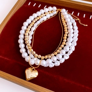 Macro detail of multi-layer baroque pearl necklace with gold heart pendant on velvet