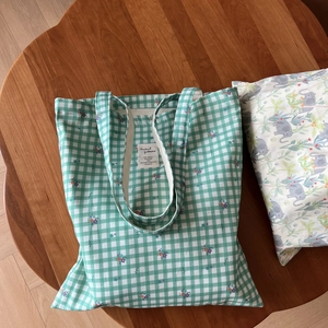 Detail of green plaid cotton tote bag with floral patterns and a woven label on wood table