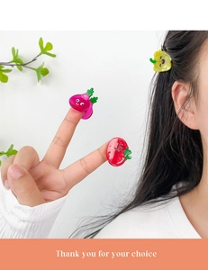 Close-up of cute cartoon strawberry and carrot mini hair claws worn on a child's hair