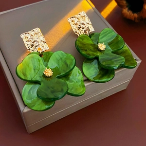 Close-up of green acrylic flower earrings with golden textured metal and petals