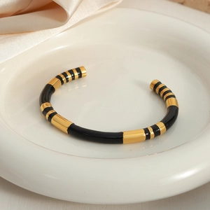 Retro gold plated stainless steel open bangle with black enamel stripes on a ceramic tray