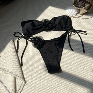 Flat lay of black bikini with mesh flower details on textured beach-style background