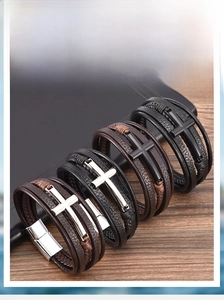 Detail of layered leather bracelets featuring metal cross charms and magnetic clasps