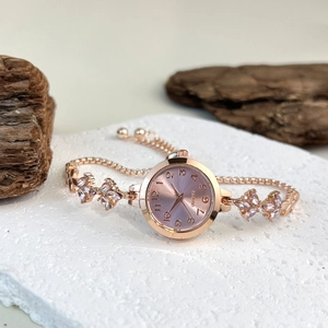 Detail of rose gold quartz watch featuring leaf-shaped crystal links on a stone surface