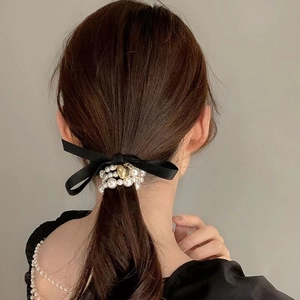 Detail showing elegant pearl hair tie with a black satin bow and golden heart pendant