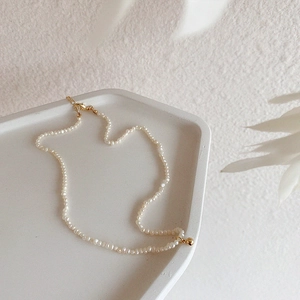 Detail of freshwater pearl necklace with gold lobster clasp on minimalist tray