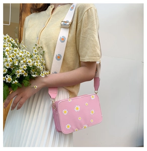 Pink crossbody bag with daisy prints and matching wide strap held by a model