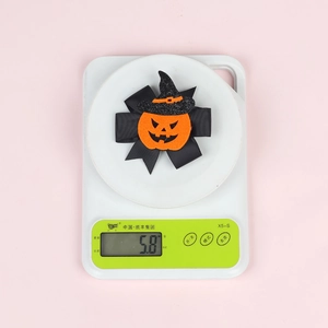 Detail shot of 5.8g Halloween pumpkin bow hair clip with witch hat on a scale