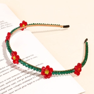 Detail of a thin gold headband featuring green beads and red crystal flower embellishments