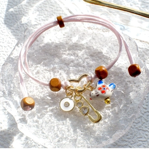 Pink hand-woven cord bracelet with ceramic bird and gold heart charm on glass tray