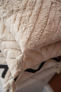 Detail of beige tufted pillow cover featuring bohemian tassels and woven cotton texture