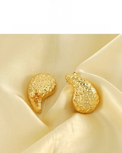 Macro detail of gold hammered teardrop earrings resting on luxurious silk fabric
