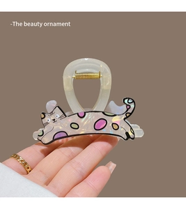 Detail view of a cream cat hair claw clip with colorful polka dots and a golden spring
