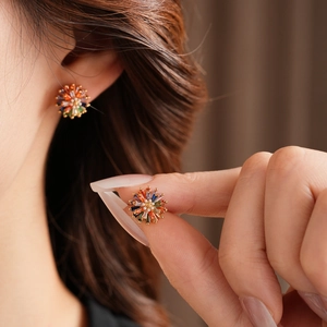Macro shot of gold flower stud earrings featuring colorful gemstones and a center pearl