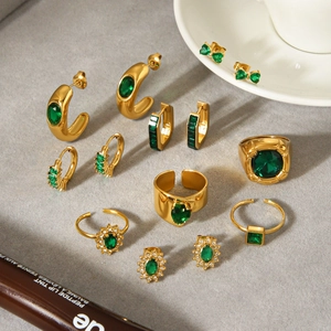 Golden jewelry set with emerald green zircon earrings and rings on light gray background