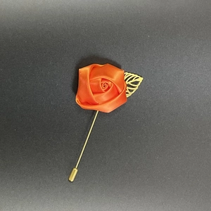 Close-up of orange satin rose lapel pin with golden metal leaf and long needle design