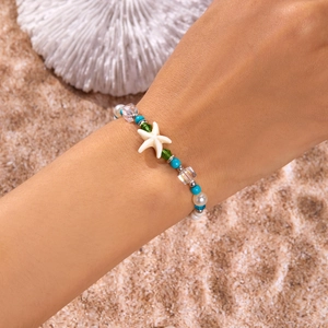 Detail shot of colorful starfish bead bracelet worn on beach with white coral