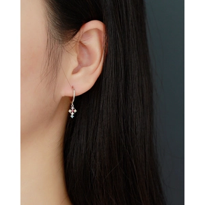 Close-up of a silver cross earring with colorful zircon stones on a female model