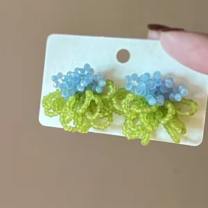 Detailed view of handmade beaded floral earrings in sky blue and green on a white display card