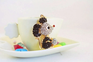 Close-up of golden mouse keychain with sparkling rhinestones on elegant white teacup background