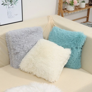 Three square plush throw pillow covers in grey, cream, and teal on a beige sofa