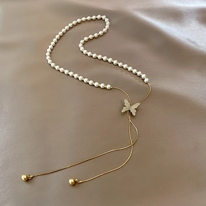 Détail du pendentif papillon doré avec perles sur un luxueux tissu en soie couleur champagne