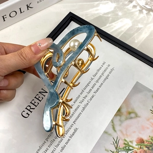 Pince à cheveux en acétate bleu avec accents métalliques dorés et perles sur fond esthétique