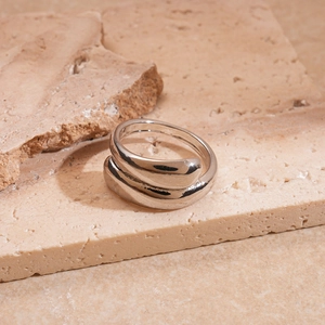 Macro shot of silver geometric wrap ring with polished metal finish on beige stone