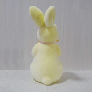 Rear view of yellow flocked Easter bunny with a pink ribbon on a gray background