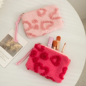Close-up of plush heart-patterned makeup bag with zipper and woven puller on white table