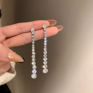 Macro detail of silver tassel earrings with sparkling rhinestones held by a hand