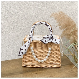 Detail of woven straw bag featuring a pearl handle and a decorative polka dot silk scarf