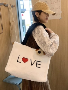 White plush tote bag with LOVE embroidery and black strap worn by a model