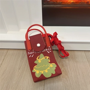 Detail of red knitted Christmas tree phone bag with Merry Christmas text on wooden floor