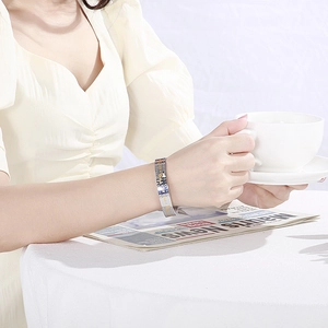 Silver stainless steel cuff bracelet with engraved patterns on a model holding a cup