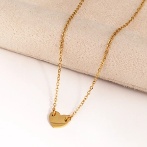 Gros plan d'un collier à pendentif cœur doré délicat posé sur un tissu beige doux