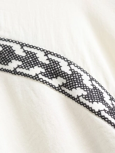 Close-up of black geometric cross-stitch embroidery on a white cotton-linen blouse fabric