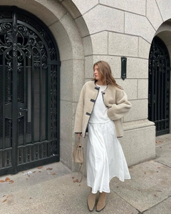 Detail of beige faux shearling jacket paired with white dress and brown handbag
