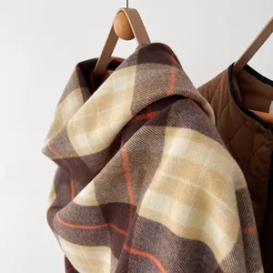 Detail of thick checkered scarf in brown and orange faux cashmere on a wooden hanger