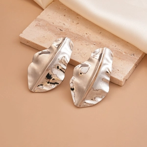 Elegant silver wrinkled leaf earrings with metallic texture on a beige stone surface