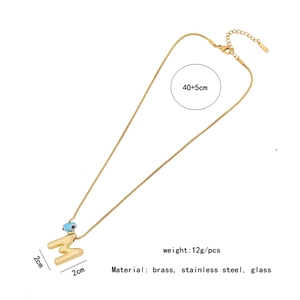Detail of gold letter M pendant with blue evil eye bead and product dimensions