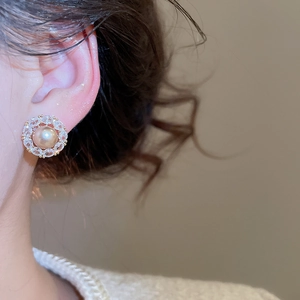Close-up of golden stud earrings featuring a champagne pearl surrounded by cubic zirconia