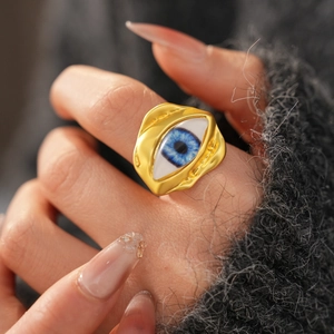 Detailed close-up of golden resin evil eye open ring on a grey knit sweater background