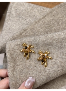 Macro shot of 18K gold plated insect earrings with brown stones on beige wool fabric