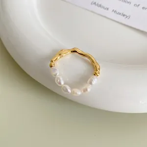 Close-up of baroque pearl and wavy gold metal ring on a minimalist ceramic plate