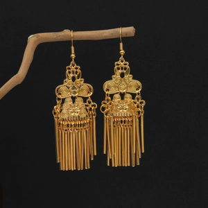 Close-up of golden ethnic tassel earrings with floral pattern on natural branches